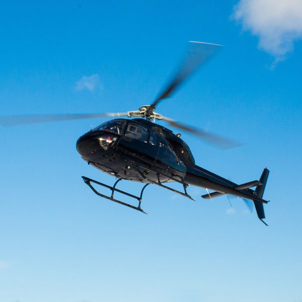 A black helicopter flies against a clear blue sky with its rotor blades spinning.
