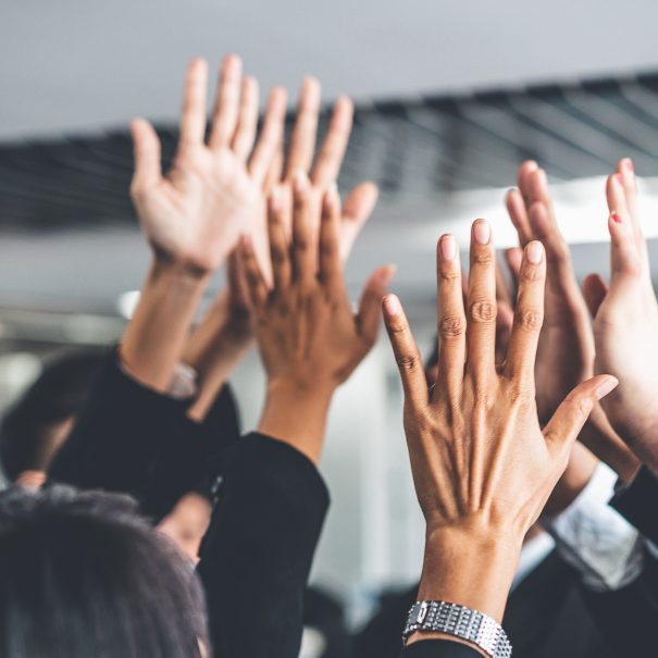 A group of people in business attire raise their hands together for a collective high five indoors.