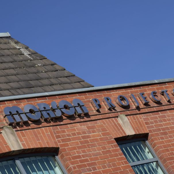 A red brick building with a tiled roof displays the sign "MORSON PROJECTS" against a clear blue sky.