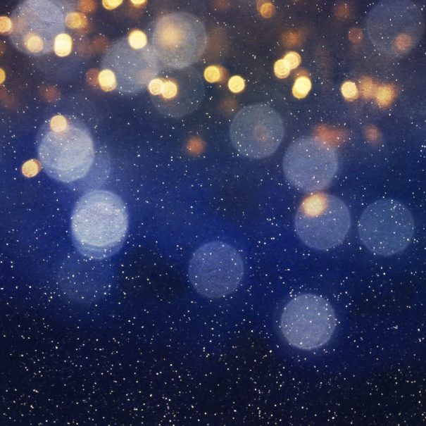 Out-of-focus golden and blue lights appear as circular bokeh shapes against a dark blue background with scattered speckles, creating an abstract, festive effect.