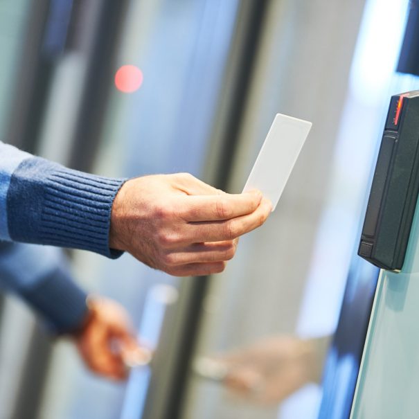 Person holding a key card and scanning it on an electronic access control reader next to a glass door.